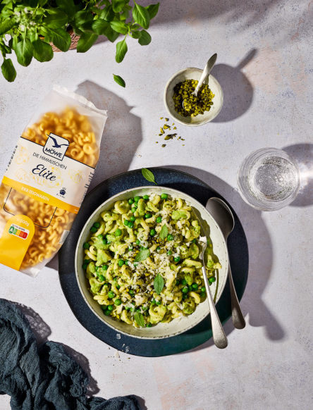 Packung Nudeln (Möwe Elite), daneben ein Teller mit Nudeln und grünem Pesto aus Erbsen.