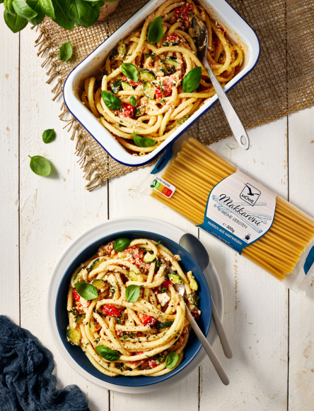 Eine Auflaufform mit Möwe Makkaroni Nudeln, die mit gebackenem Feta, Tomaten und Zucchini serviert werden. Die Packung Makkaroni darunter und dann ein gefüllter Teller. Siehe Rezept.