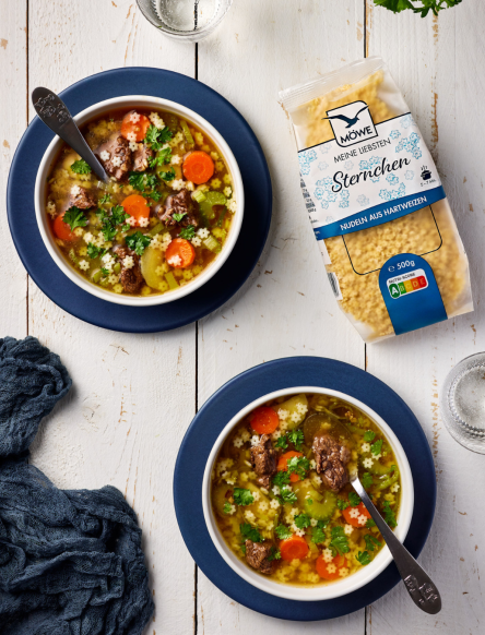 Zwei Schüsseln mit einer Gemüse-Rind-Suppe. Darin Sternchennudeln. Daneben eine Packung Möwe Meine Liebsten Sternchen Suppennudeln.