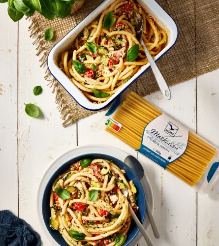 Eine Auflaufform mit Möwe Makkaroni Nudeln, die mit gebackenem Feta, Tomaten und Zucchini serviert werden. Die Packung Makkaroni darunter und dann ein gefüllter Teller. Siehe Rezept.