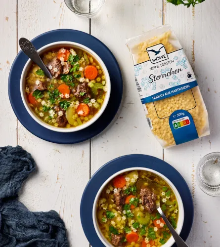 Zwei Schüsseln mit einer Gemüse-Rind-Suppe. Darin Sternchennudeln. Daneben eine Packung Möwe Meine Liebsten Sternchen Suppennudeln.