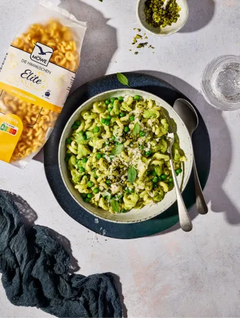 Packung Nudeln (Möwe Elite), daneben ein Teller mit Nudeln und grünem Pesto aus Erbsen.