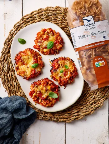 Ein heller Holzuntergrund, auf dem ein Gericht serviert wird: Vier kleine Mini Pizzen sind zu erkennen, daneben eine Packung Nudeln der Marke MÖWE Die Urigen Vollkorn-Radiatori. 